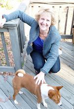 a woman kneeling down next to a brown and white dog on a wooden deck with trees in the background