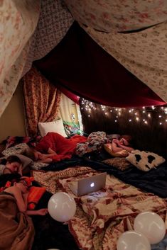 two people laying in bed under a tent with lights on the ceiling and one person using a laptop