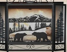 an iron fireplace screen with two bears in the woods and mountains behind it, on display