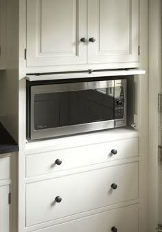 a microwave oven built into the side of a white cabinet with drawers and knobs