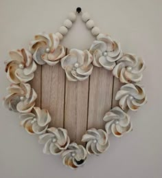 a heart shaped frame made out of seashells hangs on a wall with beads