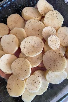 sliced potatoes in a glass dish with seasoning on top, ready to be cooked