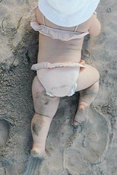 a baby in a diaper on the beach wearing a white hat and diapers