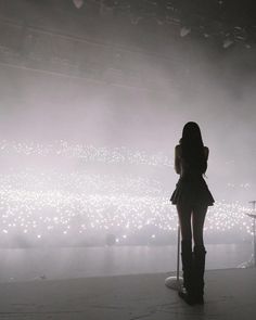 a woman standing in front of a microphone on top of a stage with lights behind her