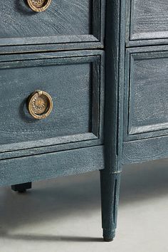 a blue dresser with brass knobs on it's doors and handles, sitting on a white surface