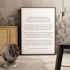 there is a framed poem on the wall next to a table with a fan and lamp