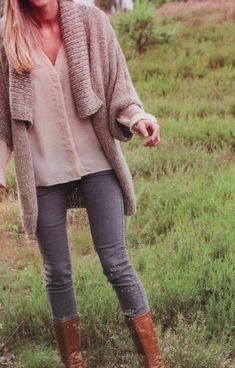 a woman is standing in the grass with her hand on her hip and wearing boots