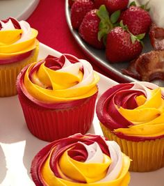 three cupcakes with yellow frosting and strawberries on the plate behind them