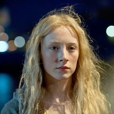 a woman with long blonde hair standing in front of a street at night, looking off to the side