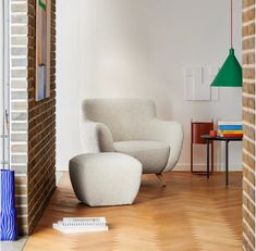 a living room with a chair, ottoman and lamp on the floor next to a brick wall