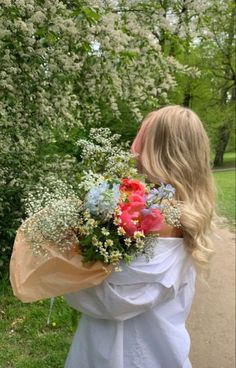 a woman in white dress holding a bouquet of flowers on sidewalk next to shrubbery