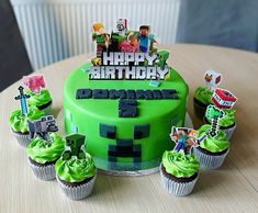 a green birthday cake with cupcakes and decorations on the table next to it