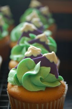 cupcakes with green and purple frosting sitting on a cooling rack