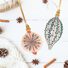 two christmas ornaments on a white table with cinnamon sticks and twine spools