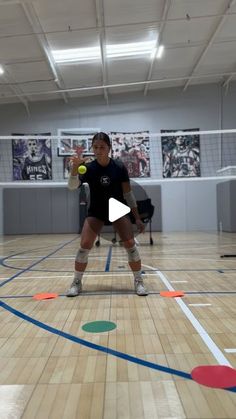 a woman in black shirt and white shorts playing with a tennis ball on an indoor court