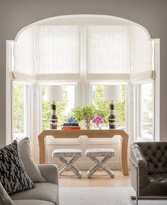 a living room with couches, chairs and tables in front of two large windows