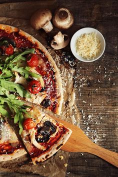 a pizza sitting on top of a wooden cutting board next to mushrooms and parmesan cheese