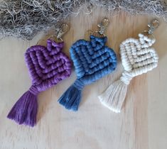 three tasselled heart shaped key chains sitting on top of a wooden table next to yarn