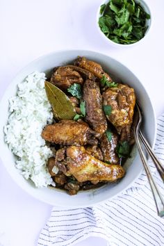 a white bowl filled with chicken and rice next to a small bowl of green leafy greens