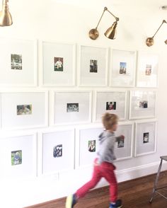 a little boy running in front of a wall with pictures on it and lights hanging from the ceiling