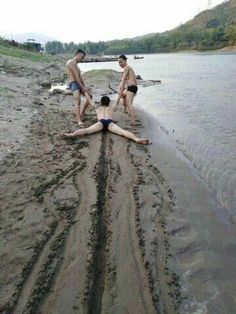 three men are playing in the mud on the beach by the water's edge