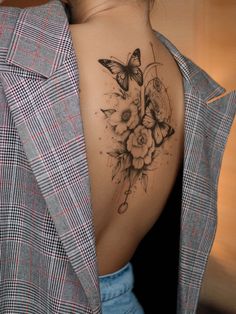 a woman's back tattoo with flowers and butterflies on her left side ribcage