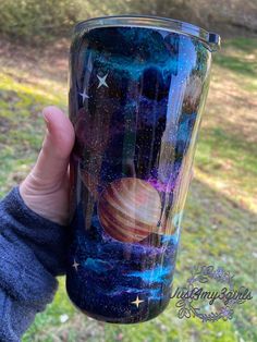 a hand holding up a cup with an image of the planets and stars on it