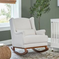 a white rocking chair sitting in a living room next to a baby crib and a potted plant