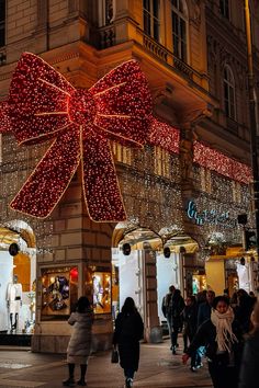 people are walking in front of a building decorated with christmas lights and a giant bow