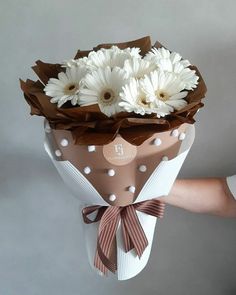 a person holding a bouquet of flowers in their left hand, with the top half wrapped in brown and white paper