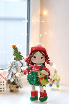 a doll is holding a teddy bear in her hand and standing next to a christmas tree