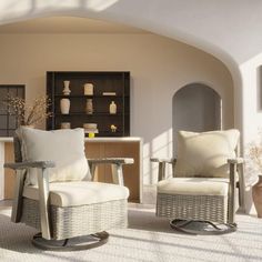 two white chairs sitting next to each other in a living room under an arch with windows