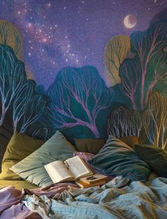 an open book sitting on top of a bed in front of a mural with trees