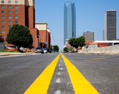 an empty street with yellow lines painted on the road and tall buildings in the background