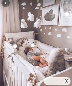 a baby sleeping in a crib with stuffed animals hanging from the ceiling and pictures on the wall