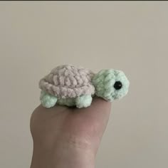 a small stuffed turtle sitting on top of a persons finger