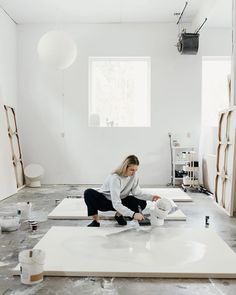 a woman sitting on top of a white floor in a room with lots of paint