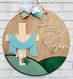 a wooden sign that says he is risen with a cross and flower on it in front of a brick wall