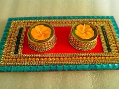 two candles are sitting on a red and blue tray with gold trimmings around them