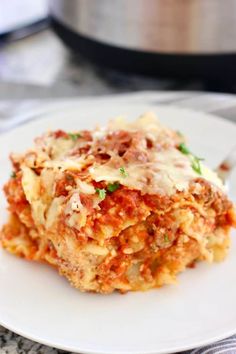 a white plate topped with lasagna next to a pot of sauce and a fork