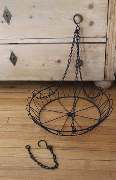 a metal basket with chains hanging from it's sides on a wooden floor next to a dresser