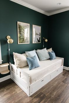 a white daybed with blue pillows in a green room next to two pictures on the wall