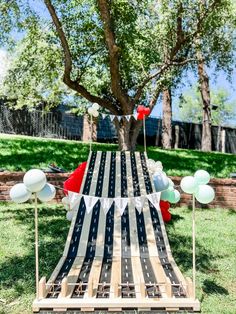 an outdoor party with balloons and streamers on the grass, in front of a tree