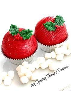 two red cupcakes decorated with holly leaves and white marshmallows on top