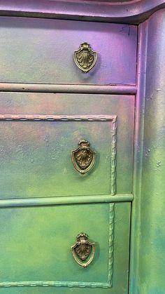 a green and purple painted dresser with two knobs on the top, one drawer open