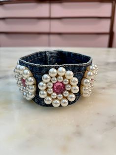 a denim cuff with pearls and pink stones on the inside is sitting on a table