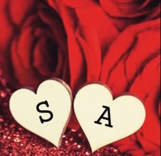 two wooden hearts with the letters sa and s on them in front of red roses