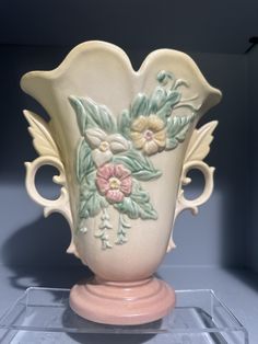 a white vase with pink and yellow flowers on it's side in a glass case