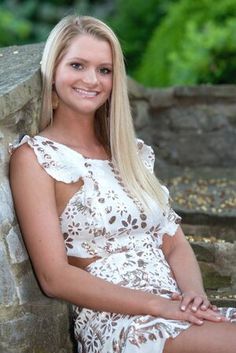 a beautiful blonde woman sitting next to a stone wall