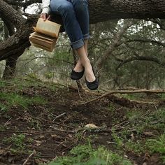 a woman sitting on top of a tree branch holding a book and wearing slippers